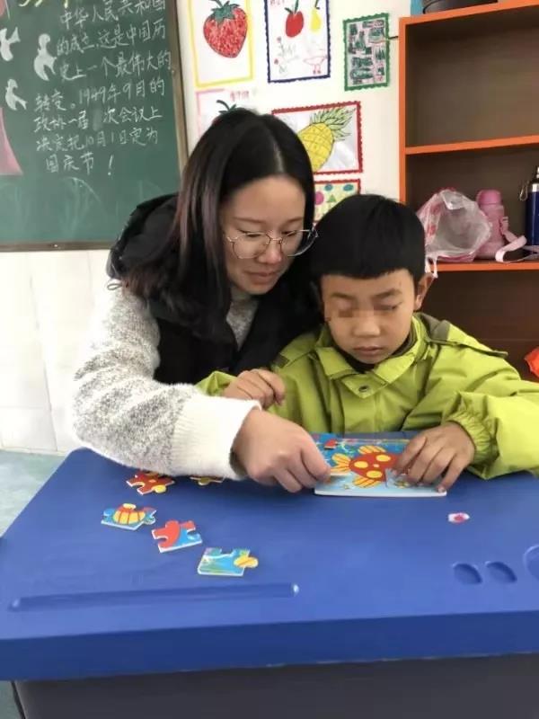 李老师正在耐心的陪自闭症的孩子玩拼图游戏