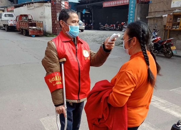 图片：残疾人志愿者邱茂春为居民测量体温